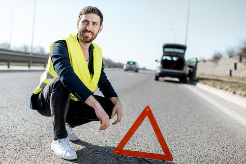 Man near the emergency sign on the roadside Portrait of a man near the emergency sign on the roadside with broken car on the background